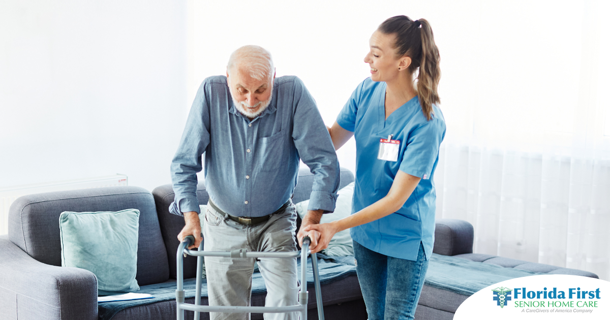 A professional caregiver helps an older man walk with a walker, showing how having a caregiver help a loved one stay mobile safely can help avoid hospital readmissions.
