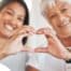 A daughter and an older mother create a heart with their hands, representing the feeling that is highlighted during National Family Caregivers Month