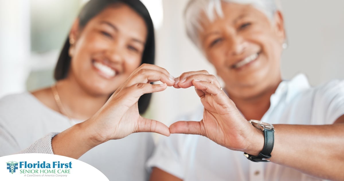 A daughter and an older mother create a heart with their hands, representing the feeling that is highlighted during National Family Caregivers Month