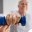 An older man is helped to lift a weight as part of physical therapy.